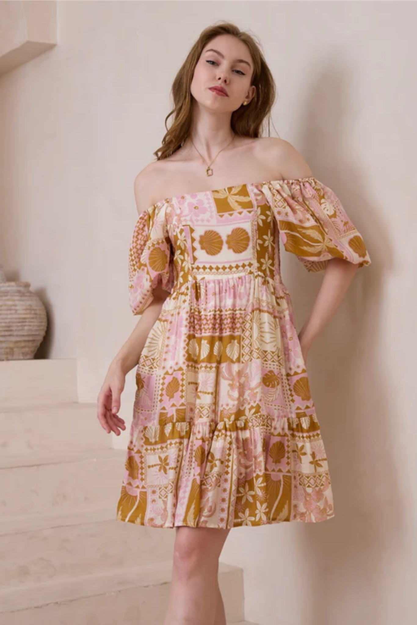 Woman wearing a pink and mustard patterned Shelley Mini Dress by Solara Boheme with elasticated shoulders and square neckline