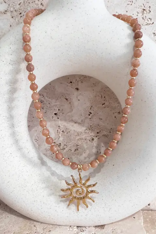 Sunrise Stone Necklace by Solara Boheme features mixed agate beads and a gold sun spiral charm on a stone display.