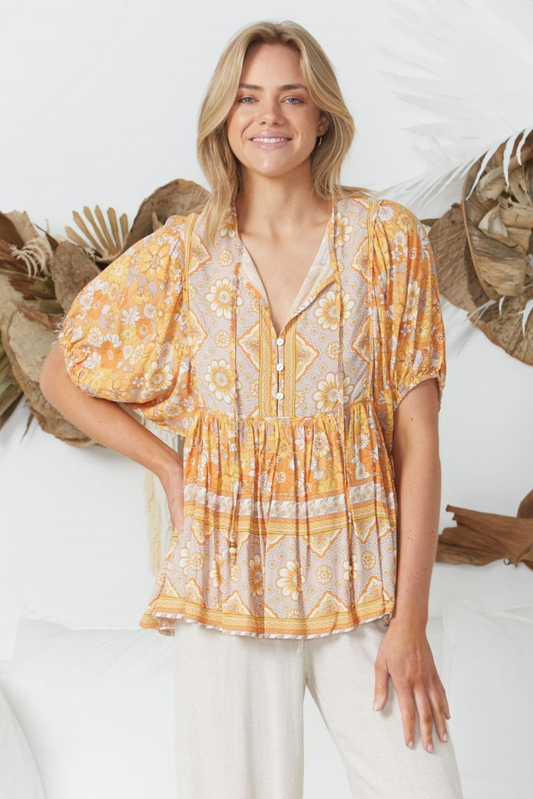Smiling woman wearing Solara Boheme Sunset Bloom Blouse with warm floral patterns and puff sleeves in bright setting