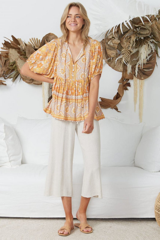 Woman wearing Solara Boheme Sunset Bloom Blouse with warm floral patterns and flowy silhouette in a bright room setting