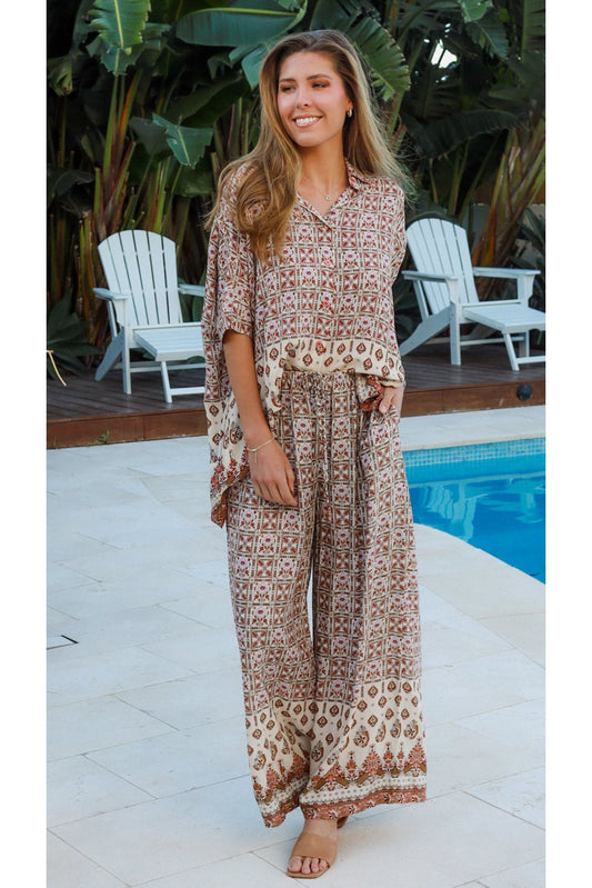 Woman wearing Tori Top by My Store standing by pool with tropical plants and lounge chairs in background