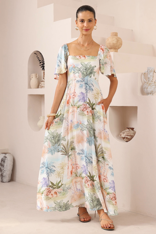 Woman wearing Solara Boheme's Tropical Escape Maxi Dress with square neckline and tropical print in a bright, minimalist room.
