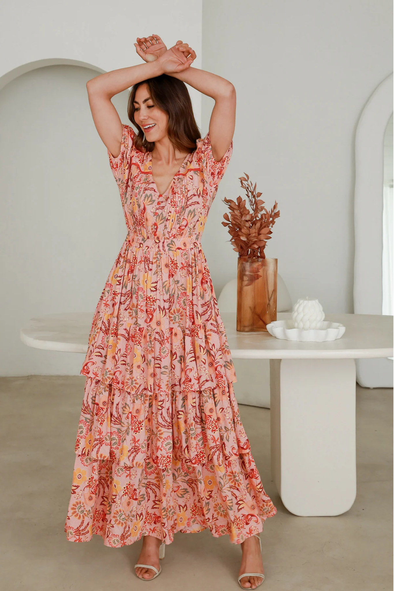 Woman wearing floral Vera Maxi Dress by Solara Boheme, standing in bright, minimalist room with arms raised above head