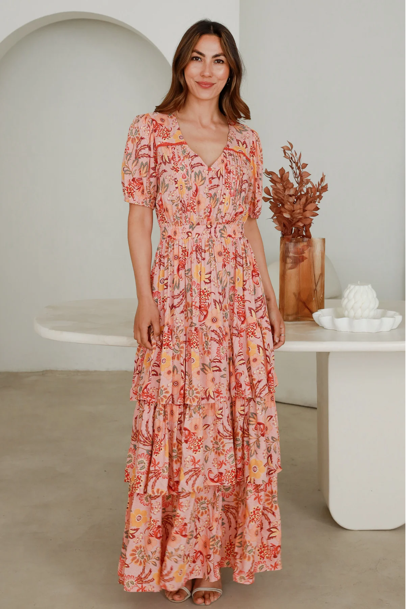Woman wearing Solara Boheme Vera Maxi Dress with floral print and tiered layers standing indoors by modern decor