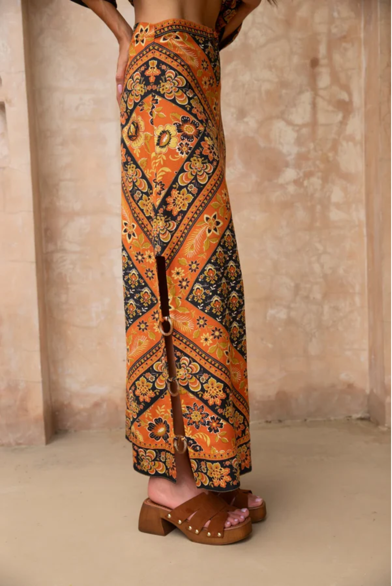 Person wearing a patterned orange and black skirt with a neutral background