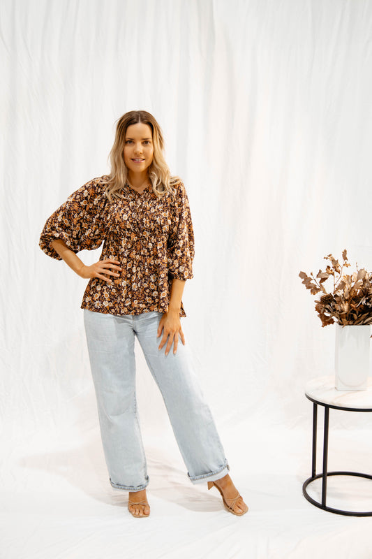Woman wearing Solara Boheme Wildflower Whisper Blouse with floral print and light denim jeans in a bright setting
