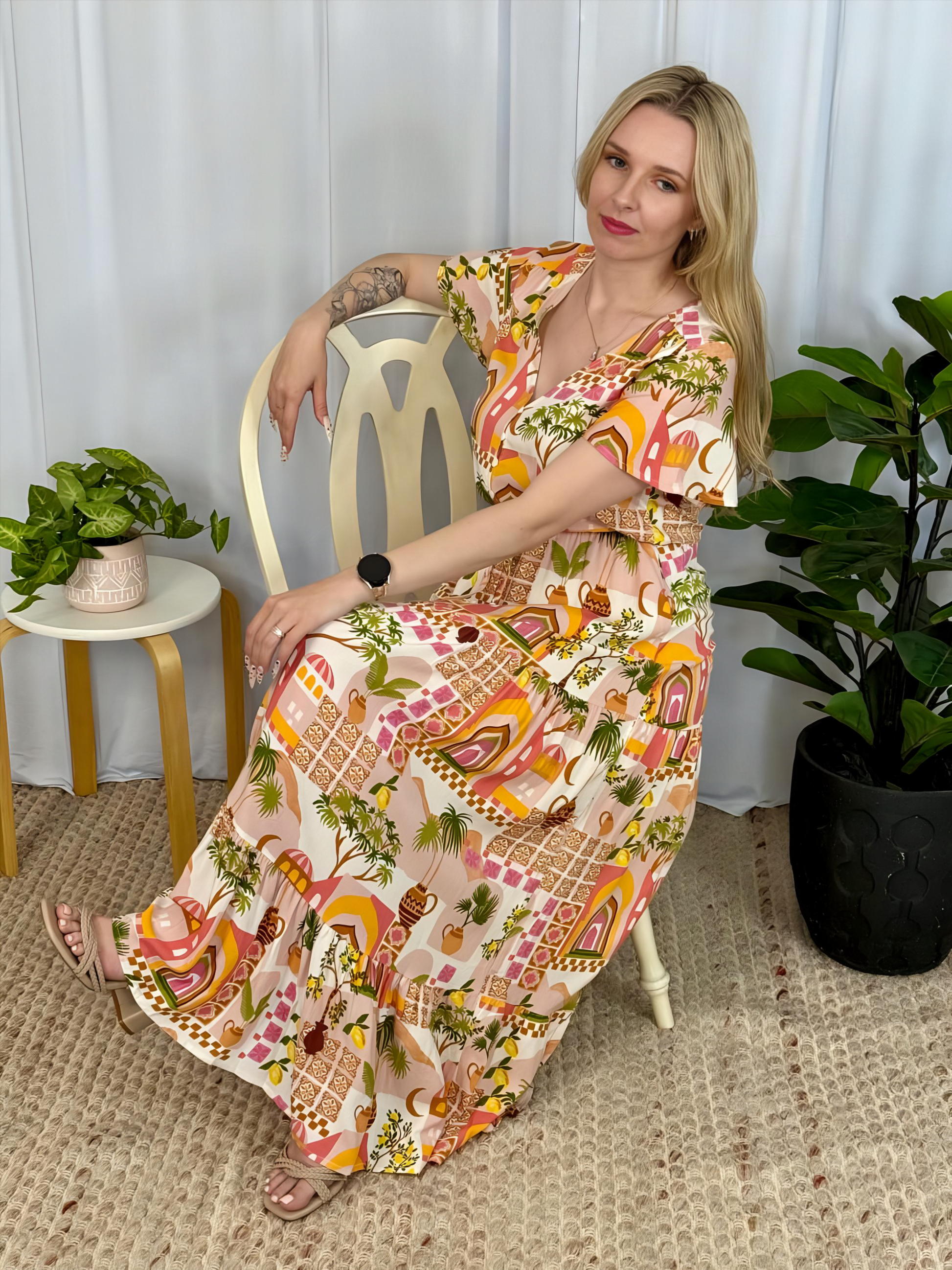 Woman seated wearing colorful Yasmin Maxi Dress by Solara Boheme with tropical print and button front bodice